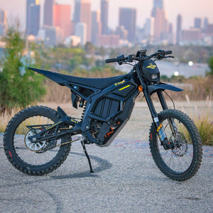 Freego Nova5 electric dirt bike parked on pavement with downtown city skyline at sunset, side view product photo