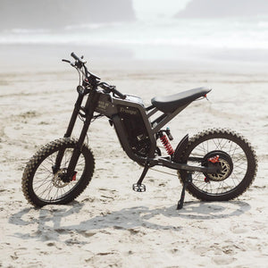 Freego electric dirt bike parked on a sandy beach, showcasing rugged off-road design against a scenic coastal backdrop.