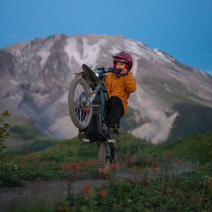 A person riding a freego nova 5 electric dirt bike wheel-up on an outdoor trail with a large mountain in the background under a blue sky