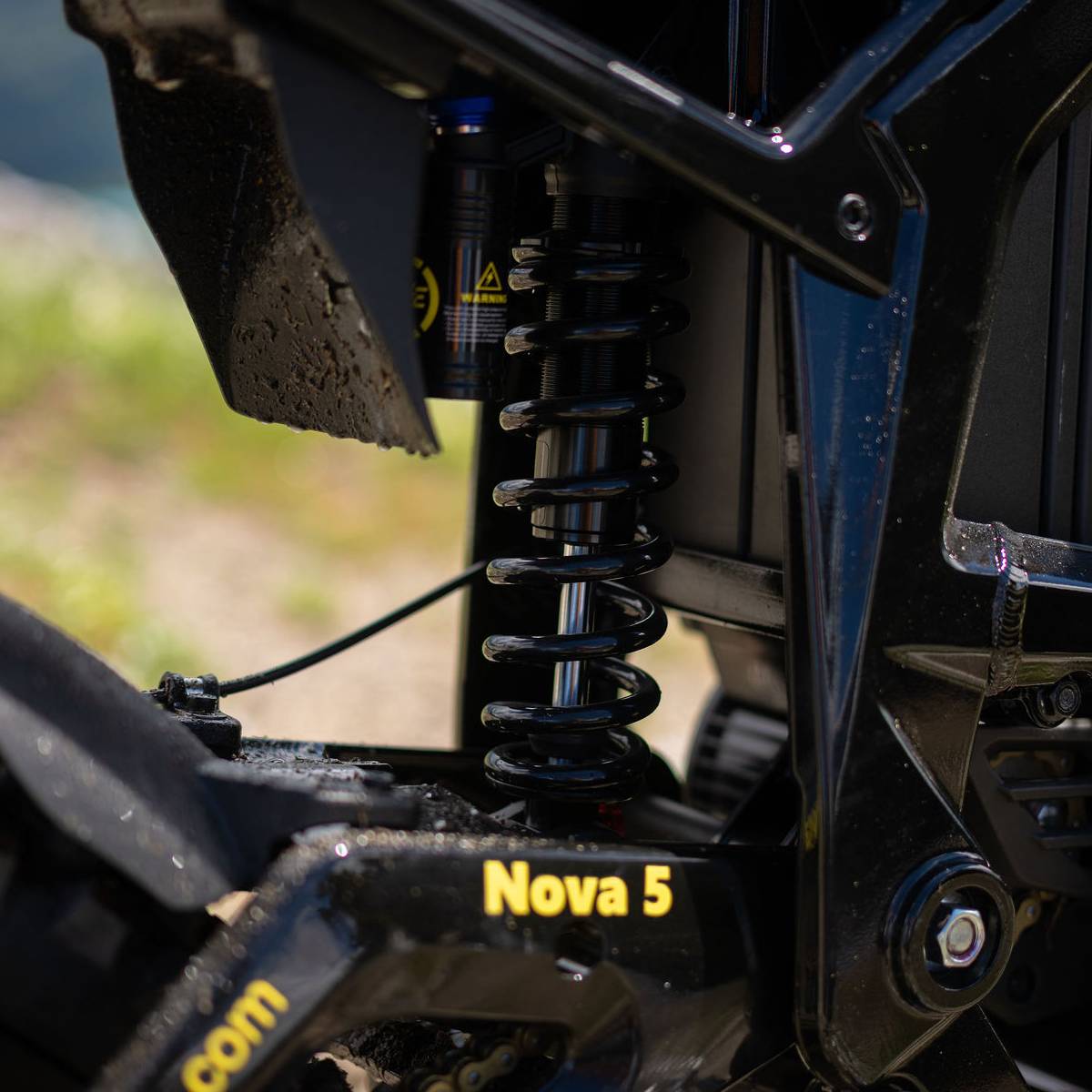 Close-up of a black freego nova 5 e-bike rear suspension shock absorber with a coil spring, mounted near the wheel area. The frame shows the model name 'Nova 5' in yellow text.