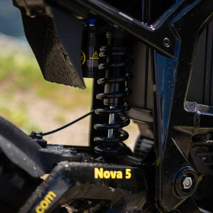 Close-up of a black freego nova 5 e-bike rear suspension shock absorber with a coil spring, mounted near the wheel area. The frame shows the model name 'Nova 5' in yellow text.