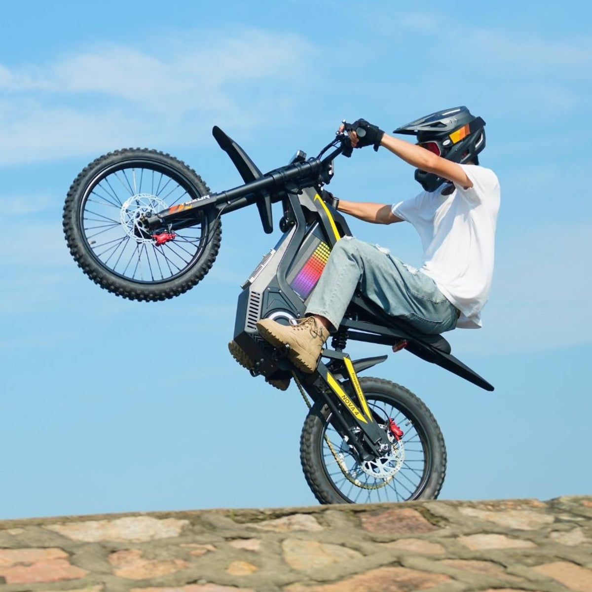 Rider performing wheelie on Freego Nova4 electric dirt bike on stone ramp under blue sky