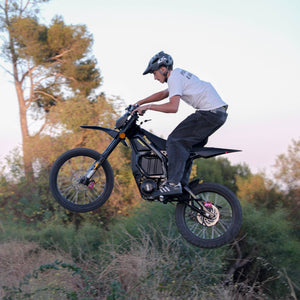 Rider airborne jumping on Freego Nova5 electric dirt bike, wooded outdoor background at dusk
