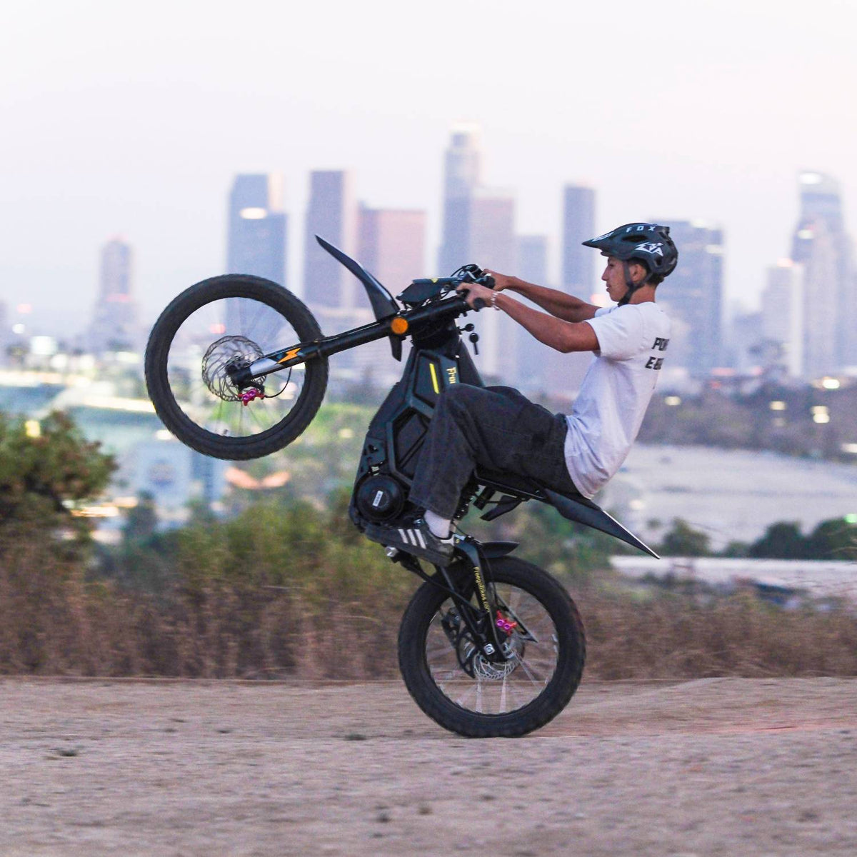 Rider performing wheelie on Freego Nova5 electric dirt bike with downtown city skyline background